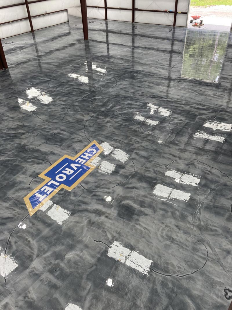Shiny gray epoxy floor with a Chevrolet logo, reflecting the interior and exterior light of the building.