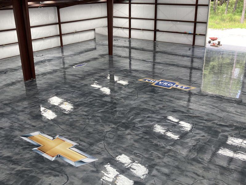 Shiny epoxy floor with Chevrolet logos in a large metal building. The floor reflects light and the building's structure.