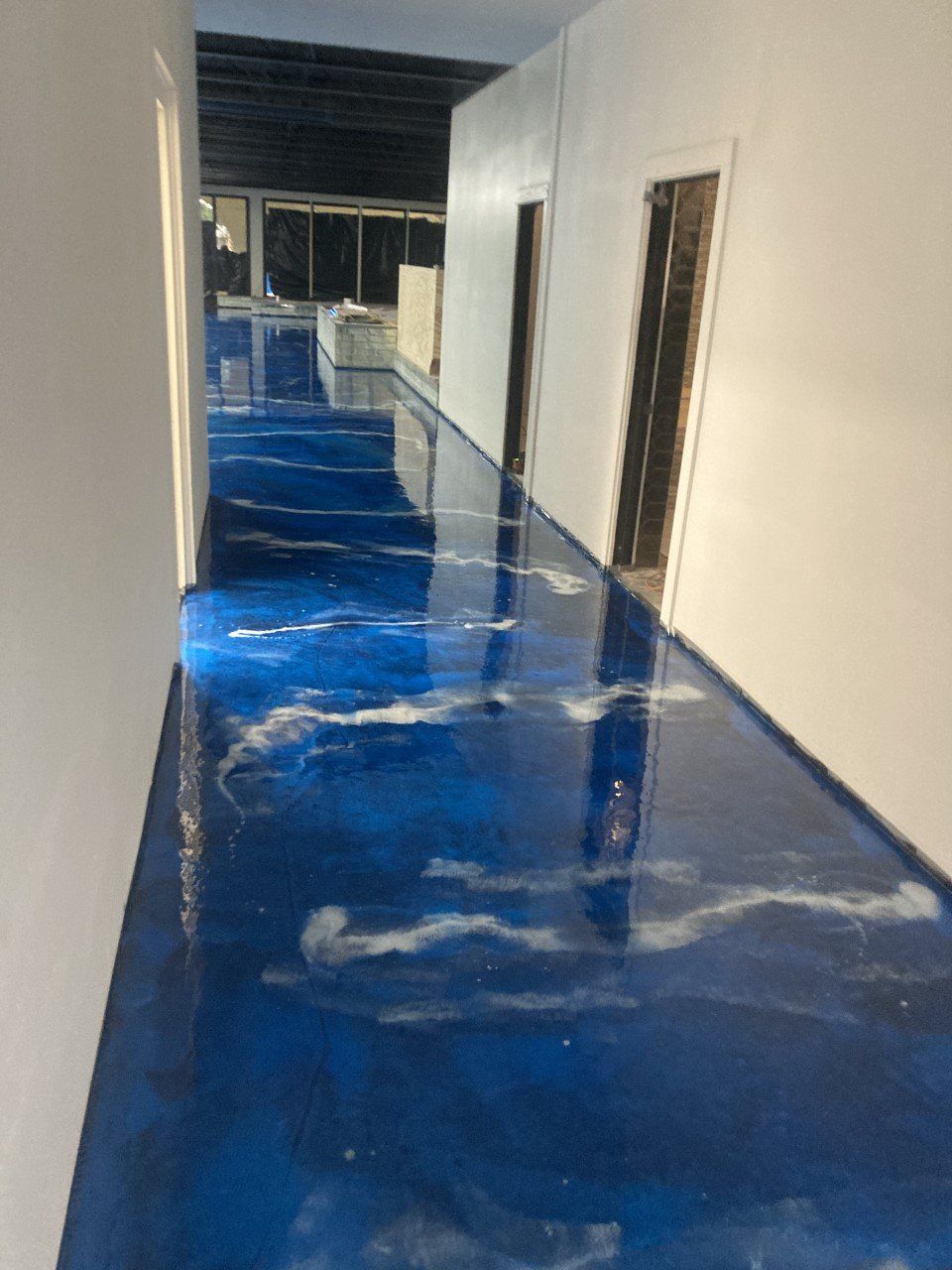 Blue and white epoxy resin floor in a hallway with white walls and two doorways.