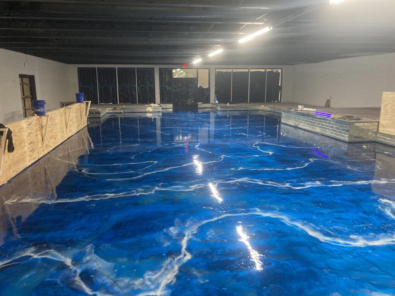 Blue and white swirled epoxy floor with a glossy finish, reflecting overhead lights. A large, empty room.