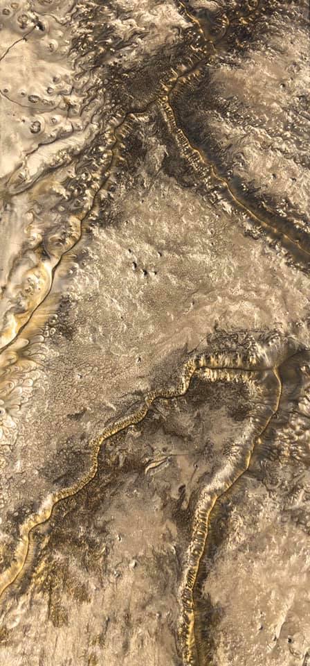 Aerial view of a textured, beige landscape with a network of golden-yellow veins.