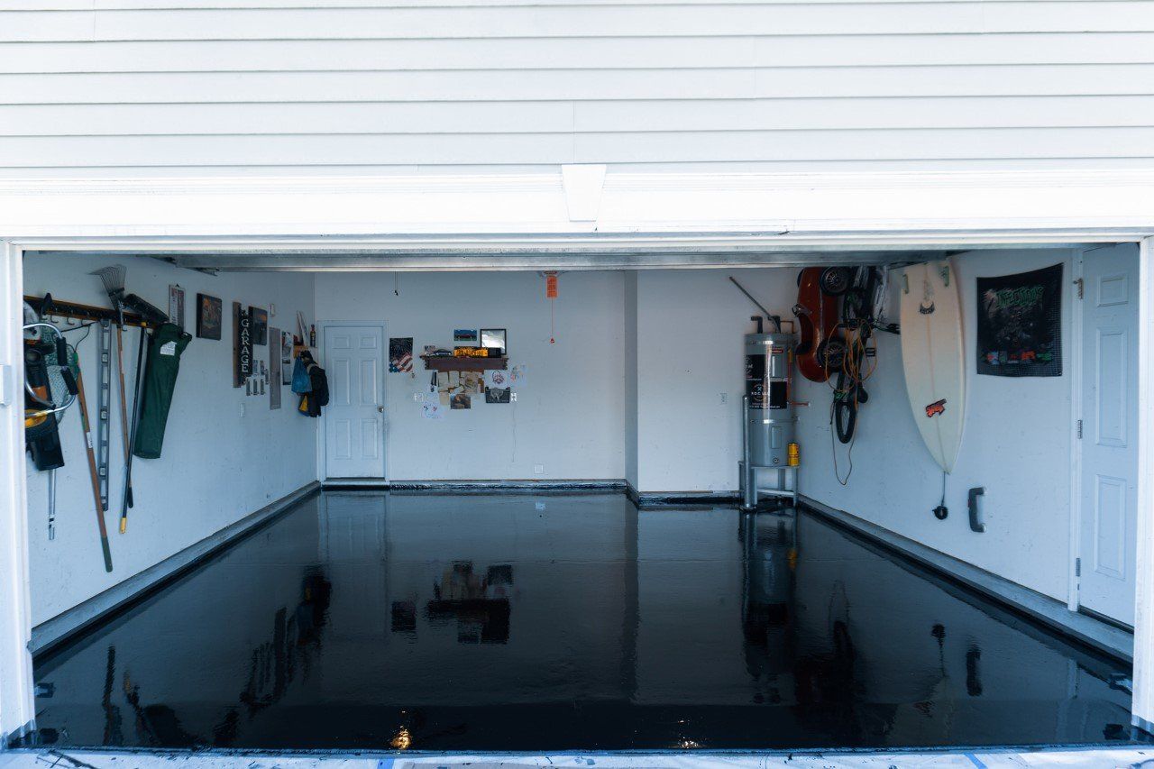 A garage interior with a glossy black floor, white walls, and the garage door open, revealing tools and equipment.