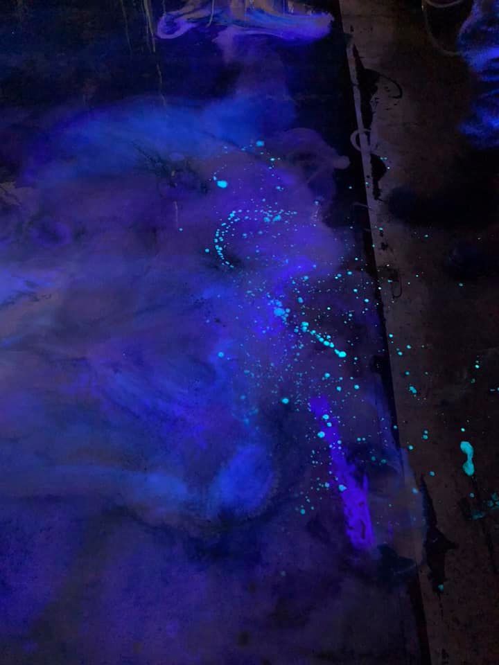 Glowing blue and turquoise pigments spread across a dark surface, creating a smoky, ethereal effect.