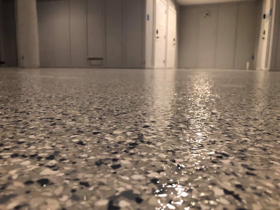 Close-up of a polished, speckled epoxy floor in a light gray color, reflecting light in a room with white paneled walls.
