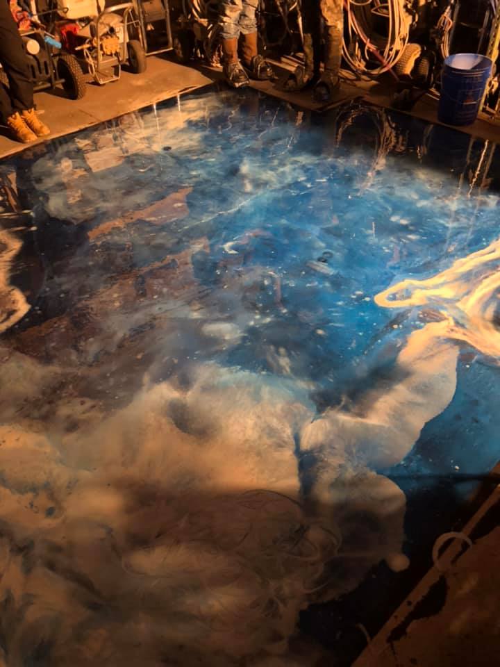 A floor being painted with swirling blue and white colors, resembling a galaxy. Several people are present.