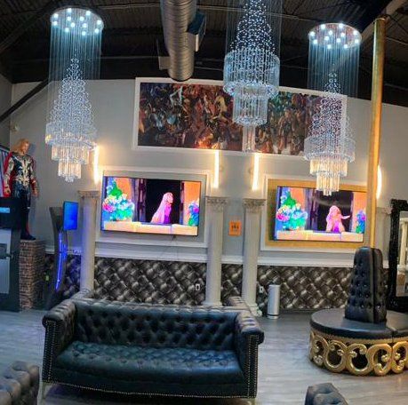 Luxurious lounge with tufted black sofas, crystal chandeliers, mirrored walls, and wall-mounted TVs