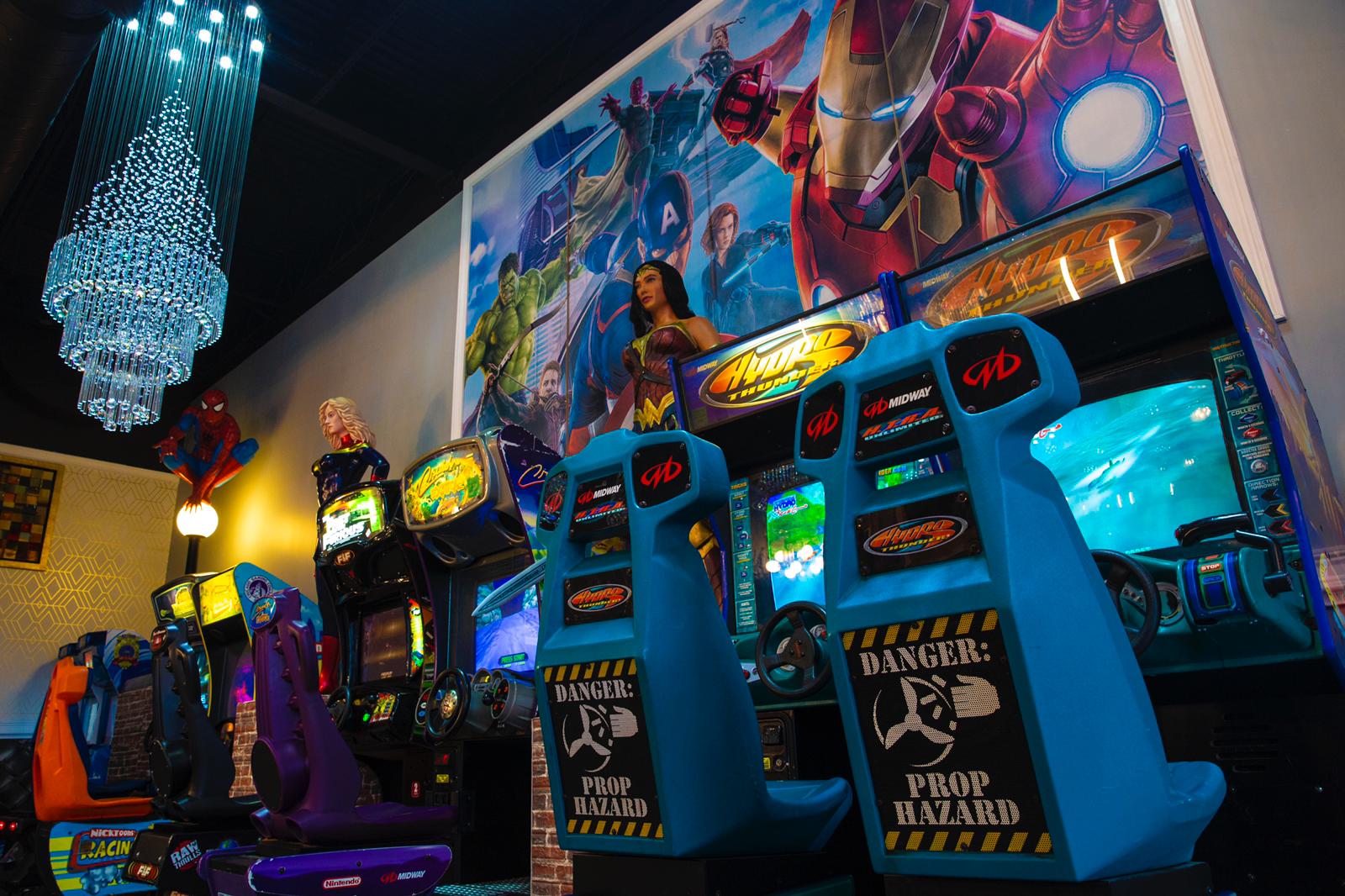 Neon-lit arcade with rows of blue game cabinets and a colorful mural overhead