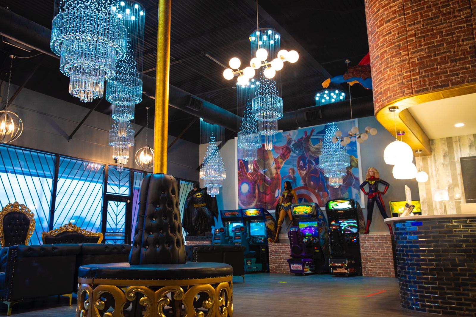 Arcade-style lounge with neon lights, hanging chandeliers, gaming machines, and brick walls