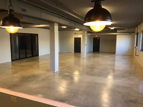 Empty industrial-style office space with polished concrete floors, white columns, and hanging black pendant lights