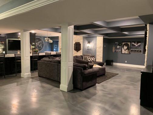 Spacious finished basement living room with gray walls, dark sofa, and polished concrete floors