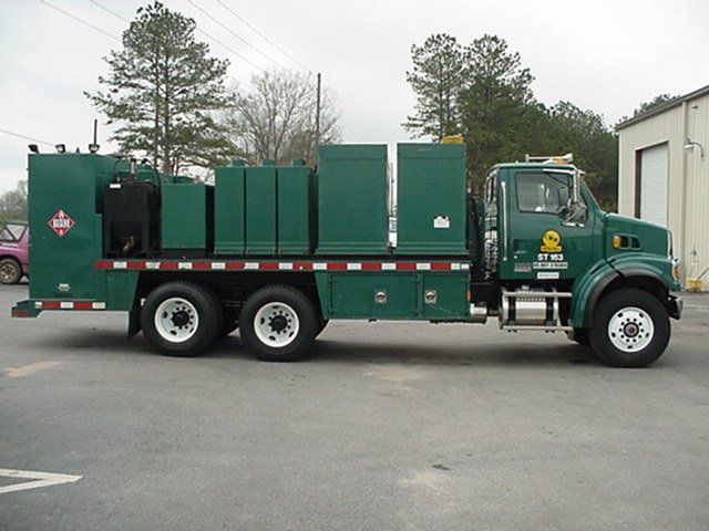 A green truck with a yellow s on the side is parked in a parking lot