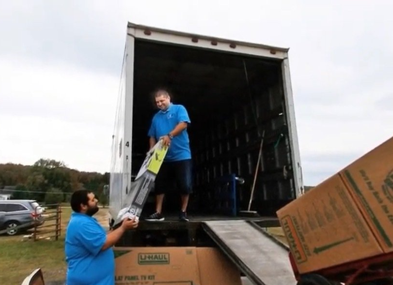 A man in a blue shirt is loading a ladder into a moving truck