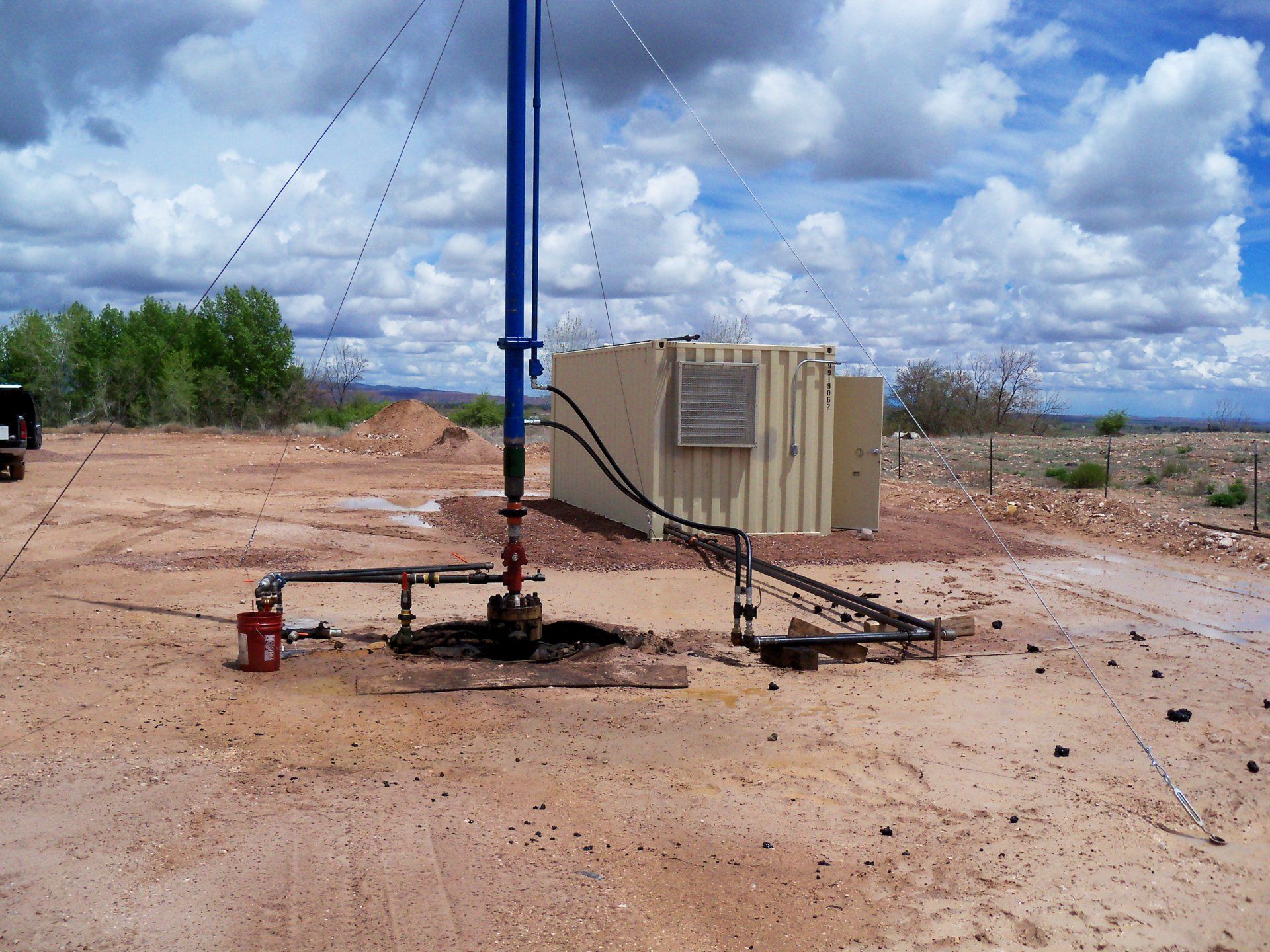 Oil drilling rig in a muddy desert area under a cloudy sky with a tan generator unit nearby