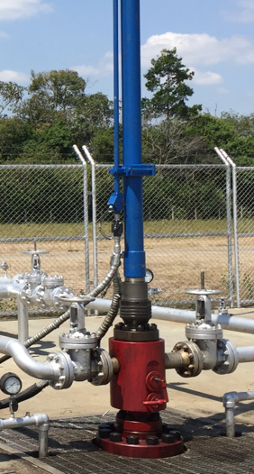 Blue and red industrial valve assembly on a metal pipeline in a grassy outdoor field