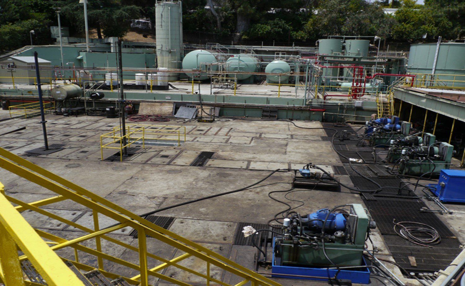Industrial yard with pipes, tanks, and scaffolding under construction in a fenced outdoor area