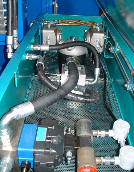 Close-up of turquoise industrial machinery with hoses, wiring, and metal components inside a compartment