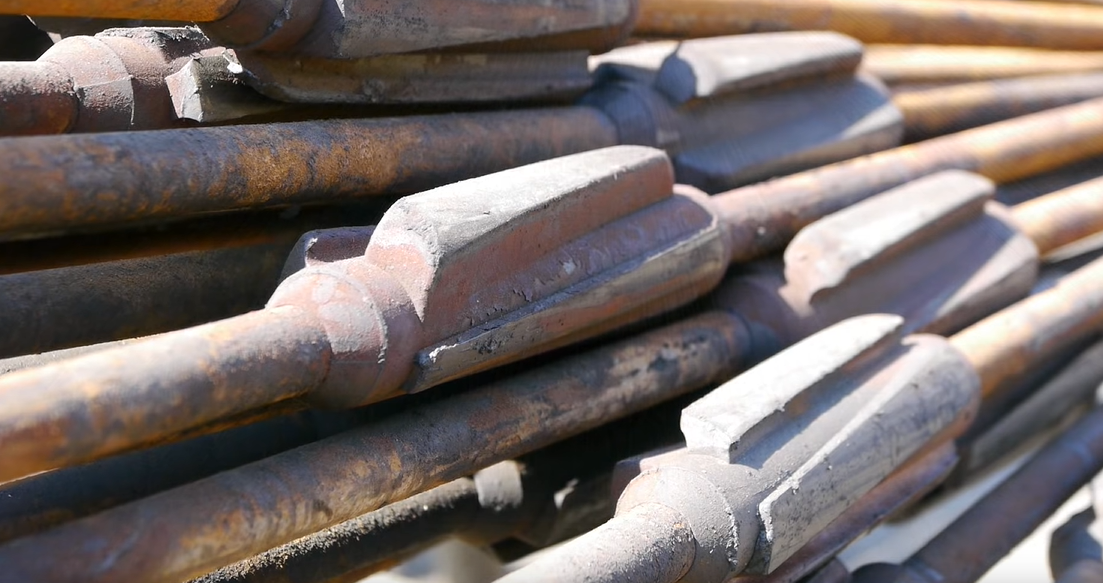 Stacked metal railroad spikes with rust and white residue, viewed in close-up.