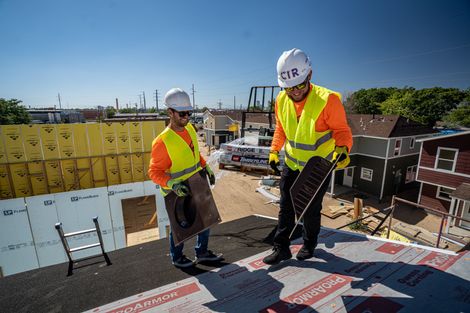 Two construction workers are working on the roof of a building.