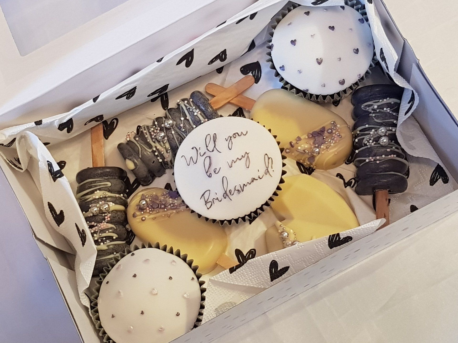 A box filled with cupcakes and a sign that says `` will you be my bridesmaid ''
