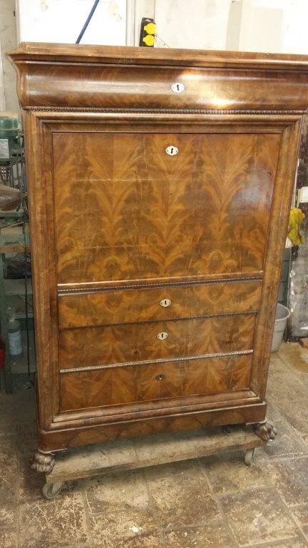 Antiker Holzschrank mit eingelegtem Furnier und zwei Schubladen, stehend auf dem Boden einer Werkstatt.