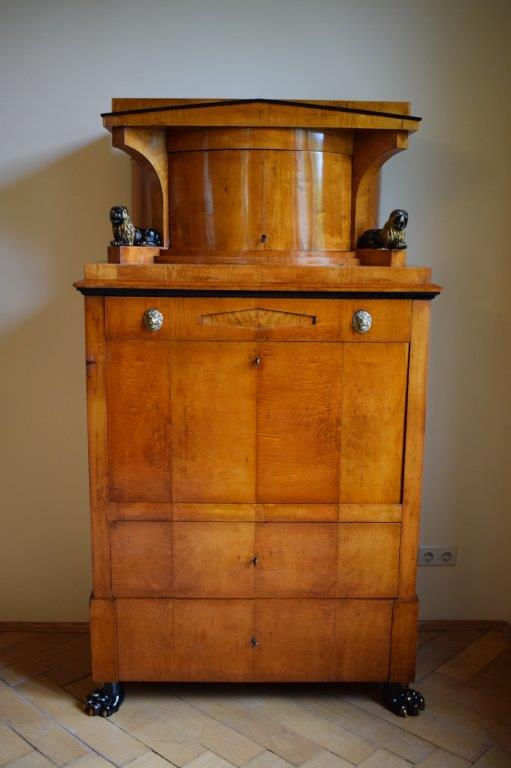 Ein Holzschrank mit runder Platte und kleinen Figuren, der auf Rollen an einer schlichten Wand steht.