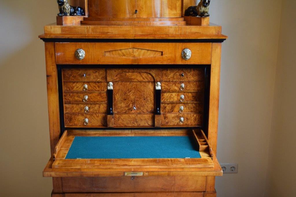 Antiker Holzschrank mit kleinen Schubladen und einer blauen, mit Filz ausgekleideten Schreibfläche, an einer Wand.