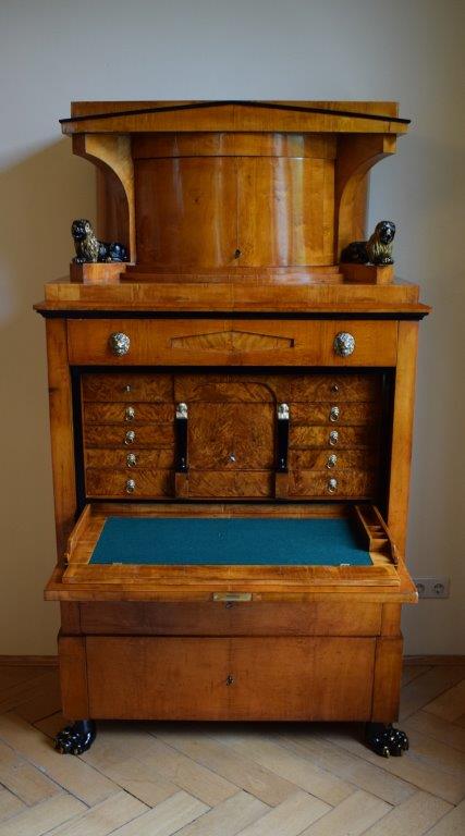 Antiker Holzschrank mit verzierten Schubladen und einem blau ausgekleideten Fach, fotografiert in Innenräumen.