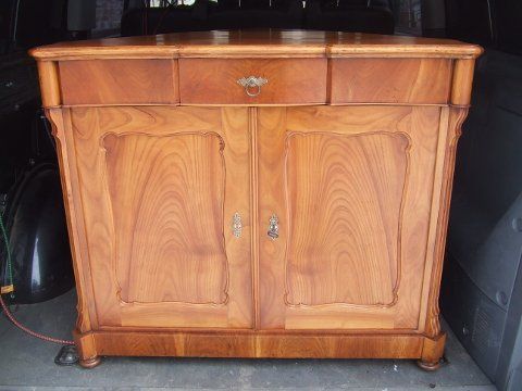 Ein Holzschrank mit zwei Türen und einer Schublade, der sich im hinteren Teil eines Fahrzeugs befindet.