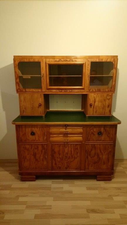 Holzschrank mit Glastüren und Schubladen, auf einem hellen Holzboden.
