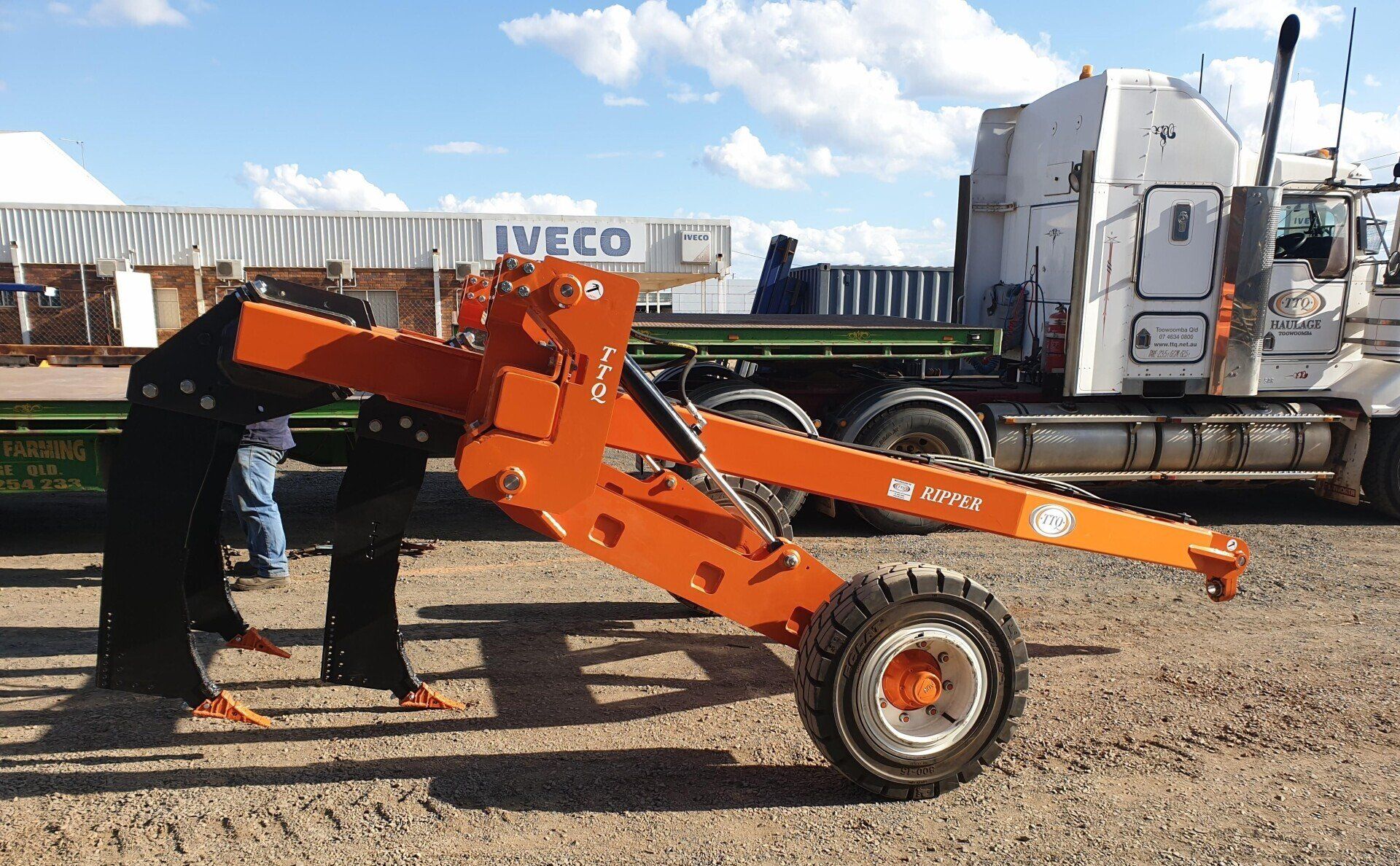 A TTQ Tree Line Ripper sitting on gravel next to a truck.