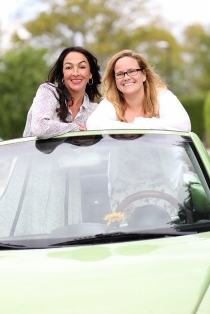 Zwei Frauen posieren in einem grünen Auto für ein Foto.