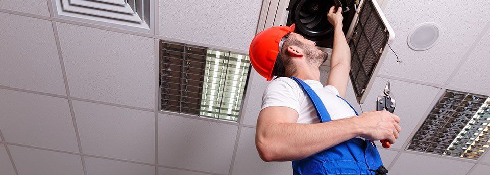 Operaio su una scala che ripara un  impianto di condizionamento industriale