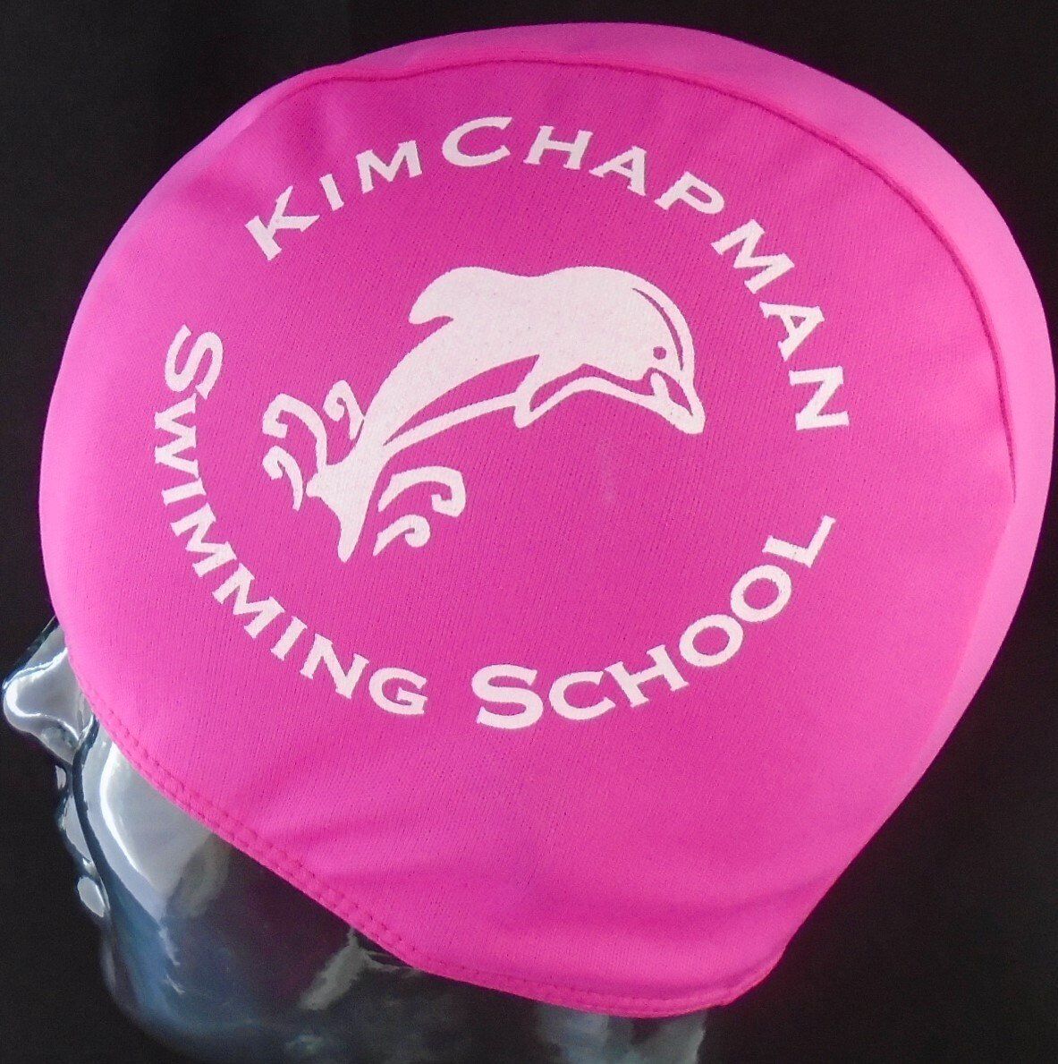 A pink swim cap that says kim chapman swimming school
