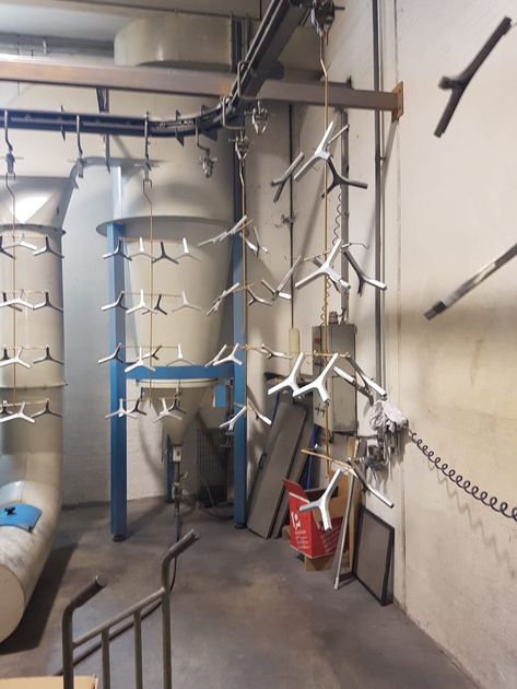 Locale tecnico industriale con tubature, telai di supporto blu, catene sospese e un secchio rosso vicino al muro.