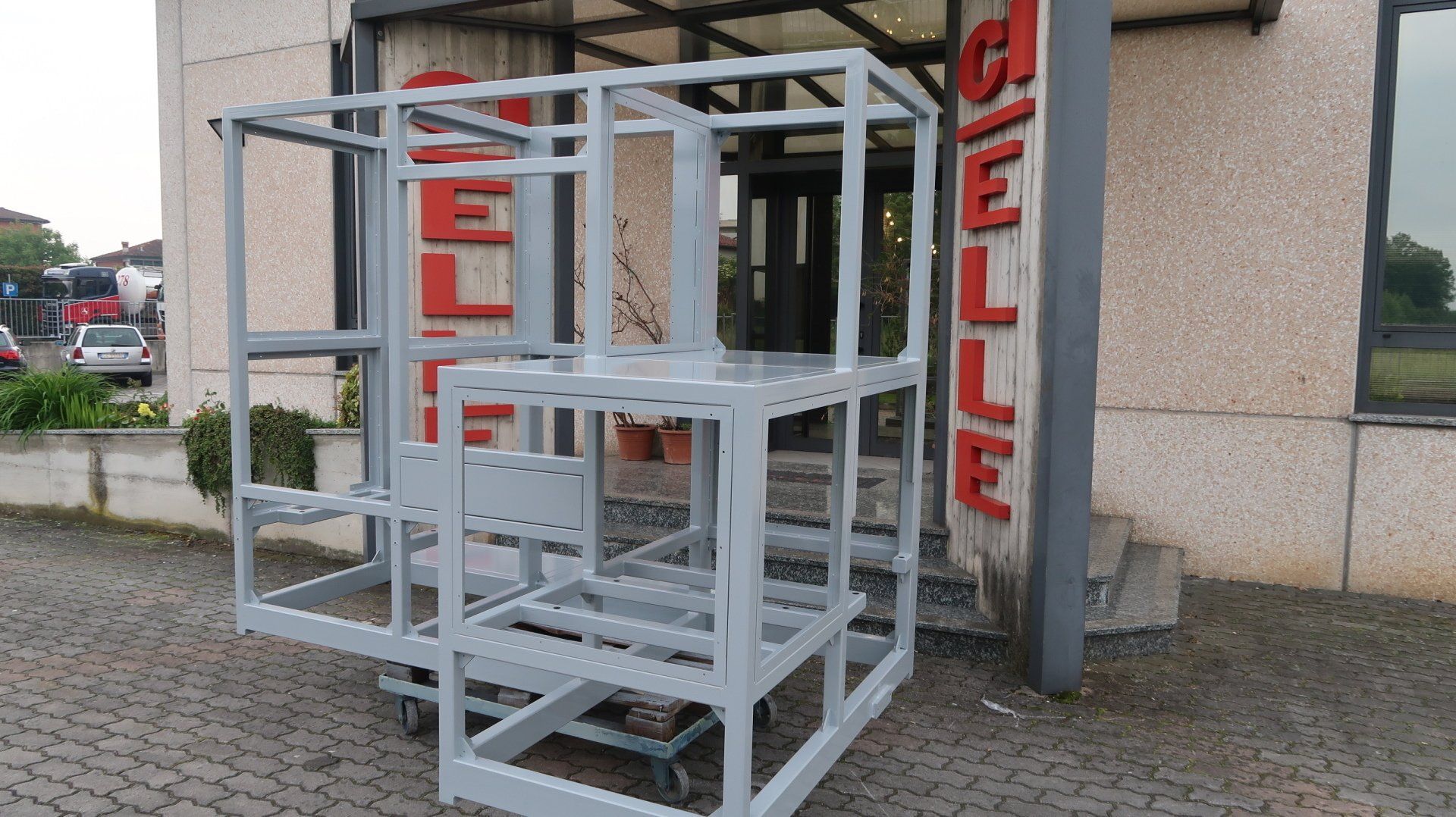 Recinzione con struttura metallica bianca all'esterno di un edificio, con insegne verticali rosse con la scritta 