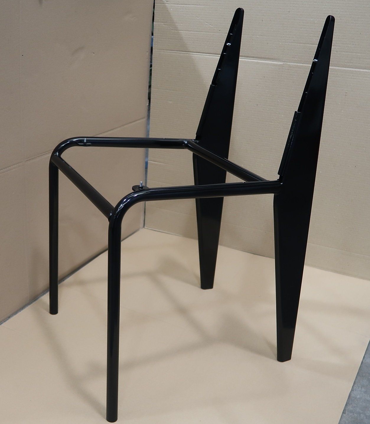 Sedia moderna nera con struttura quadrata aperta e due alti supporti angolari per lo schienale, addossata a una parete beige.