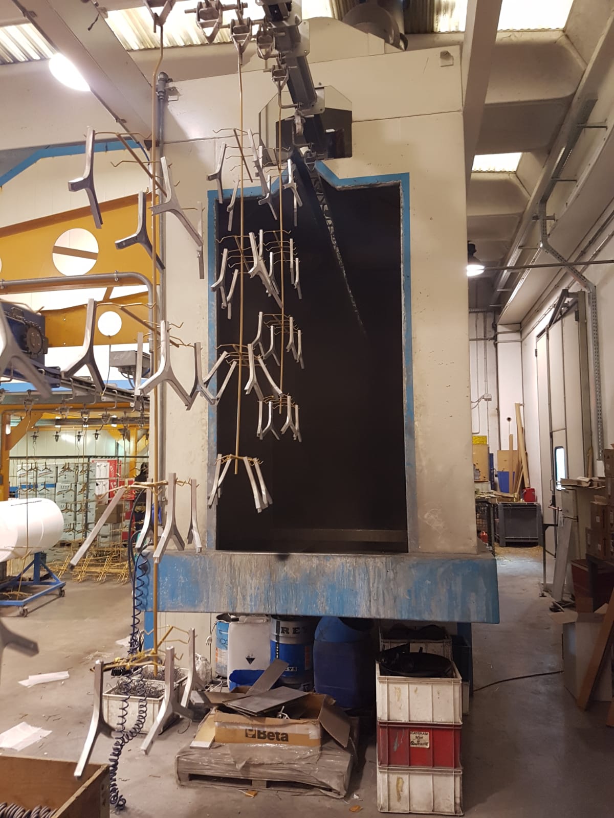 Macchinario industriale in una fabbrica, con cavi pendenti e una struttura metallica blu accanto a un'apertura rettangolare scura.