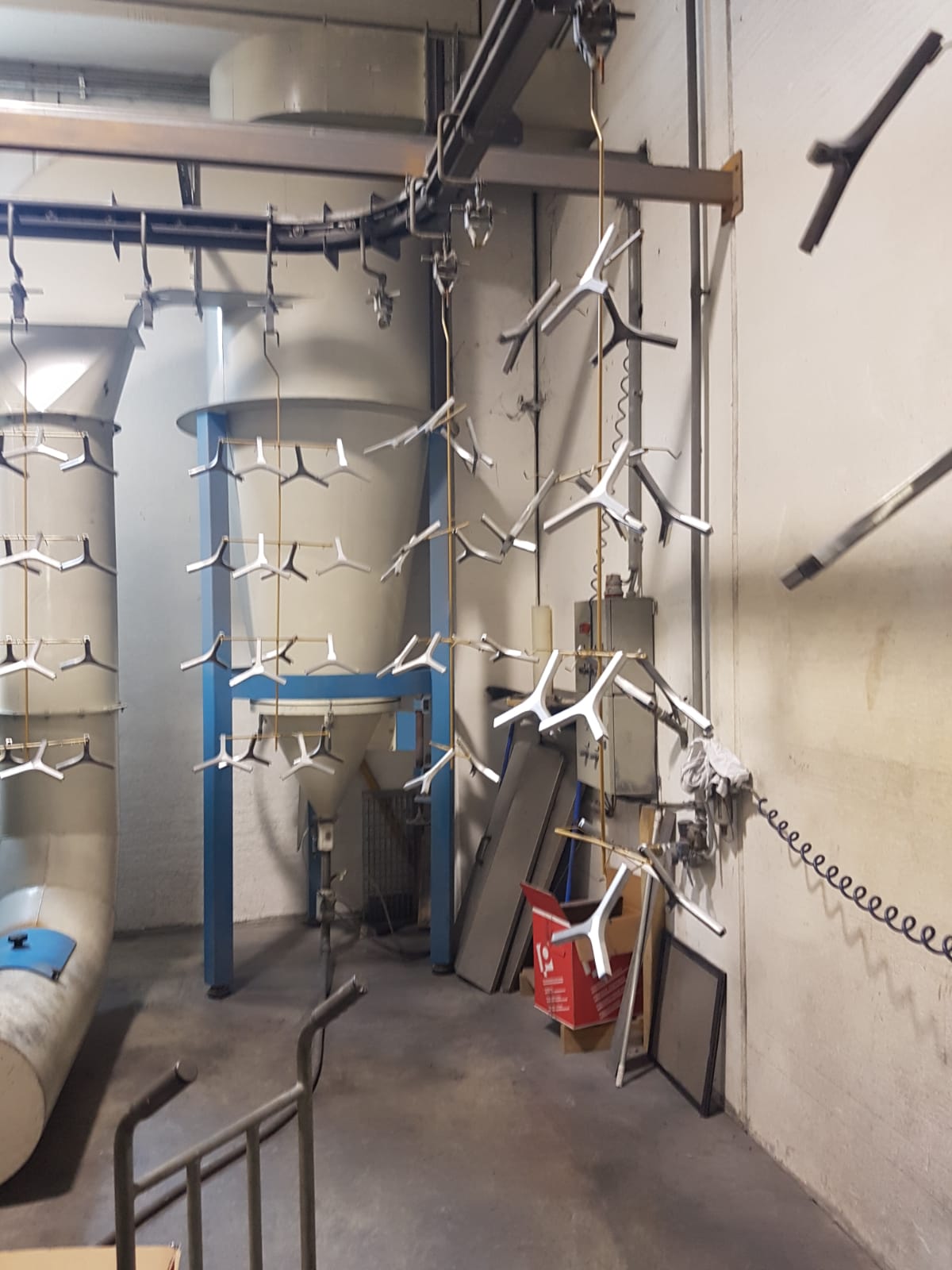 Locale industriale con tubature, pannelli fonoassorbenti bianchi sospesi e un macchinario con struttura blu in uno stretto corridoio.