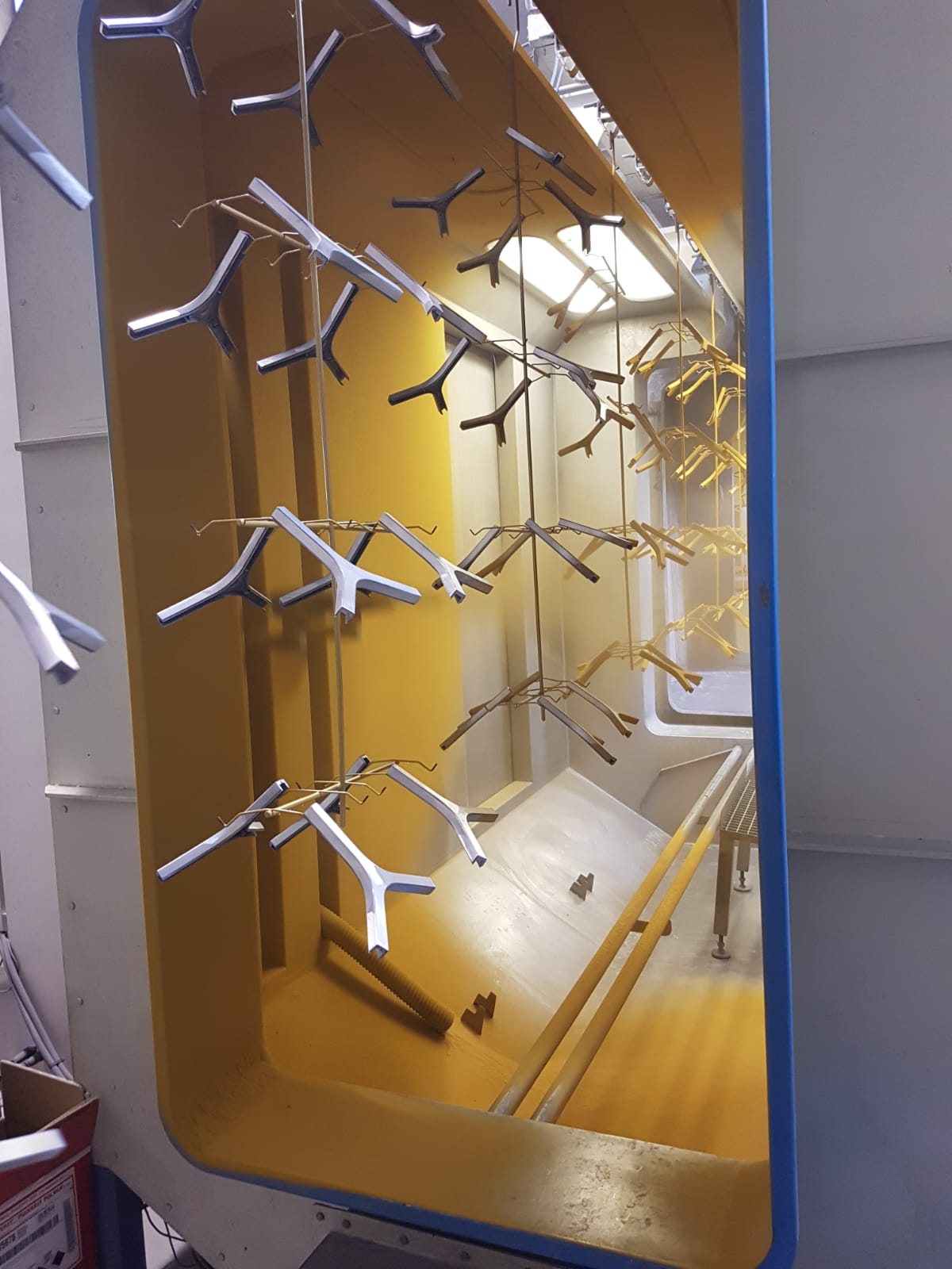 Camera industriale vuota di colore giallo con ugelli di spruzzatura in metallo e componenti in plastica bianca sul pavimento.