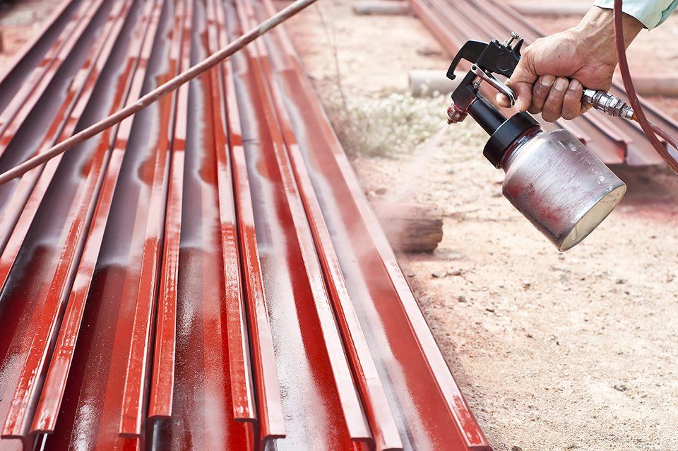 Un operaio spruzza vernice rossa su tubi metallici impilati all'aperto.