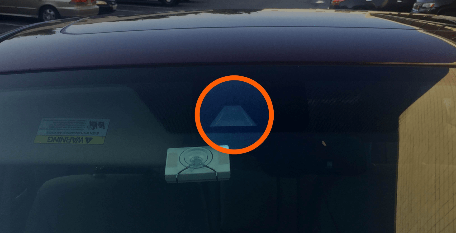 A close-up of a car windshield showing an orange circle highlighting a camera sensor mounted behind the glass.