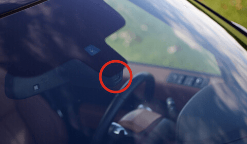A close-up of a vehicle's windshield housing, with a red circle highlighting the integrated forward-facing camera lens.