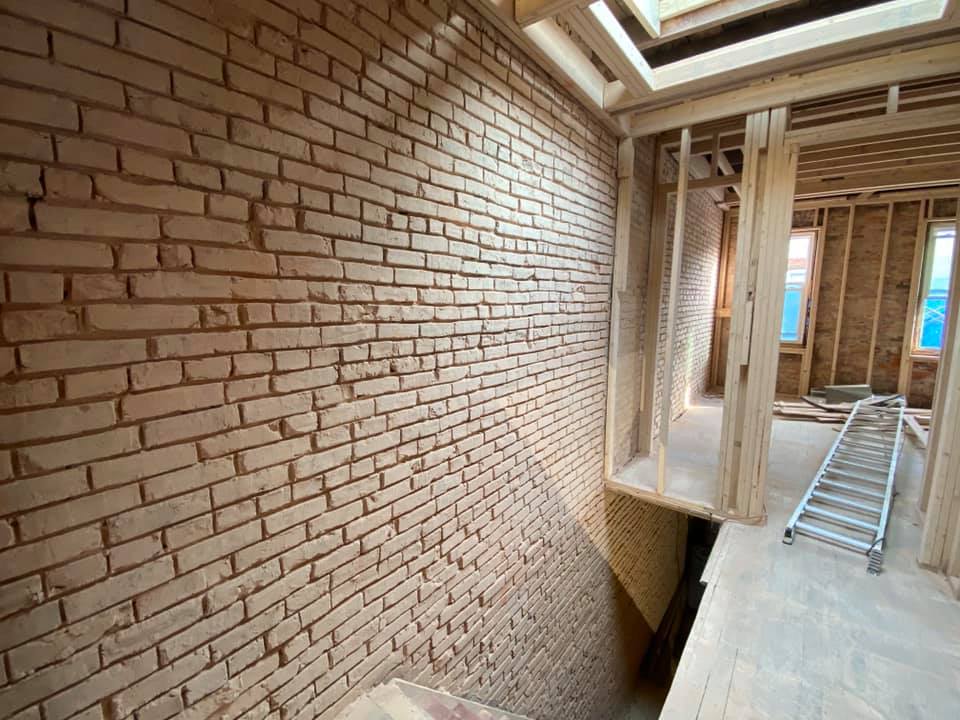 Interior of a building under construction. Exposed brick wall, wooden framing, open doorways, and a ladder.