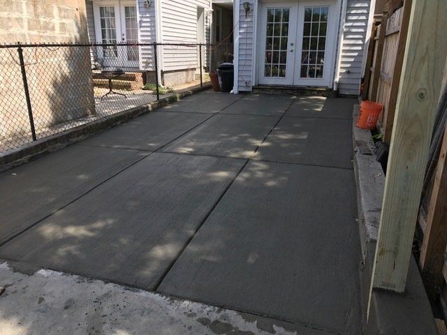A freshly poured concrete patio next to a house with French doors. The patio is sectioned with seams.