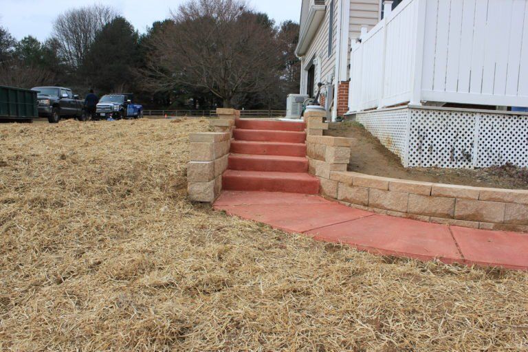 Brick steps and walkway leading to a house with a white fence, in a grassy yard.