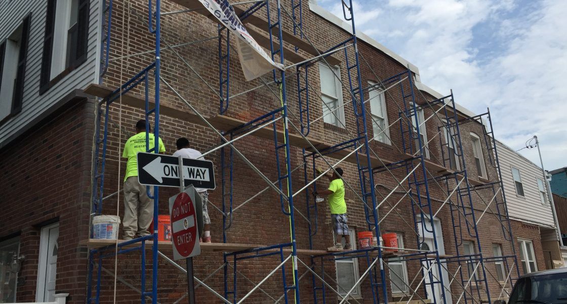 Brick building under renovation with scaffolding and workers painting.