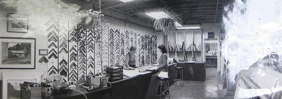 Black and white photo of a frame shop interior with frames on display and two people at a counter.