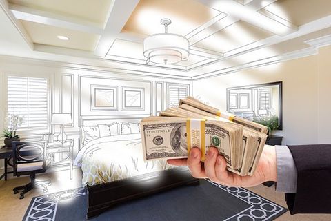 A hand holds stacks of $100 bills in front of an unfinished rendering of a bedroom.