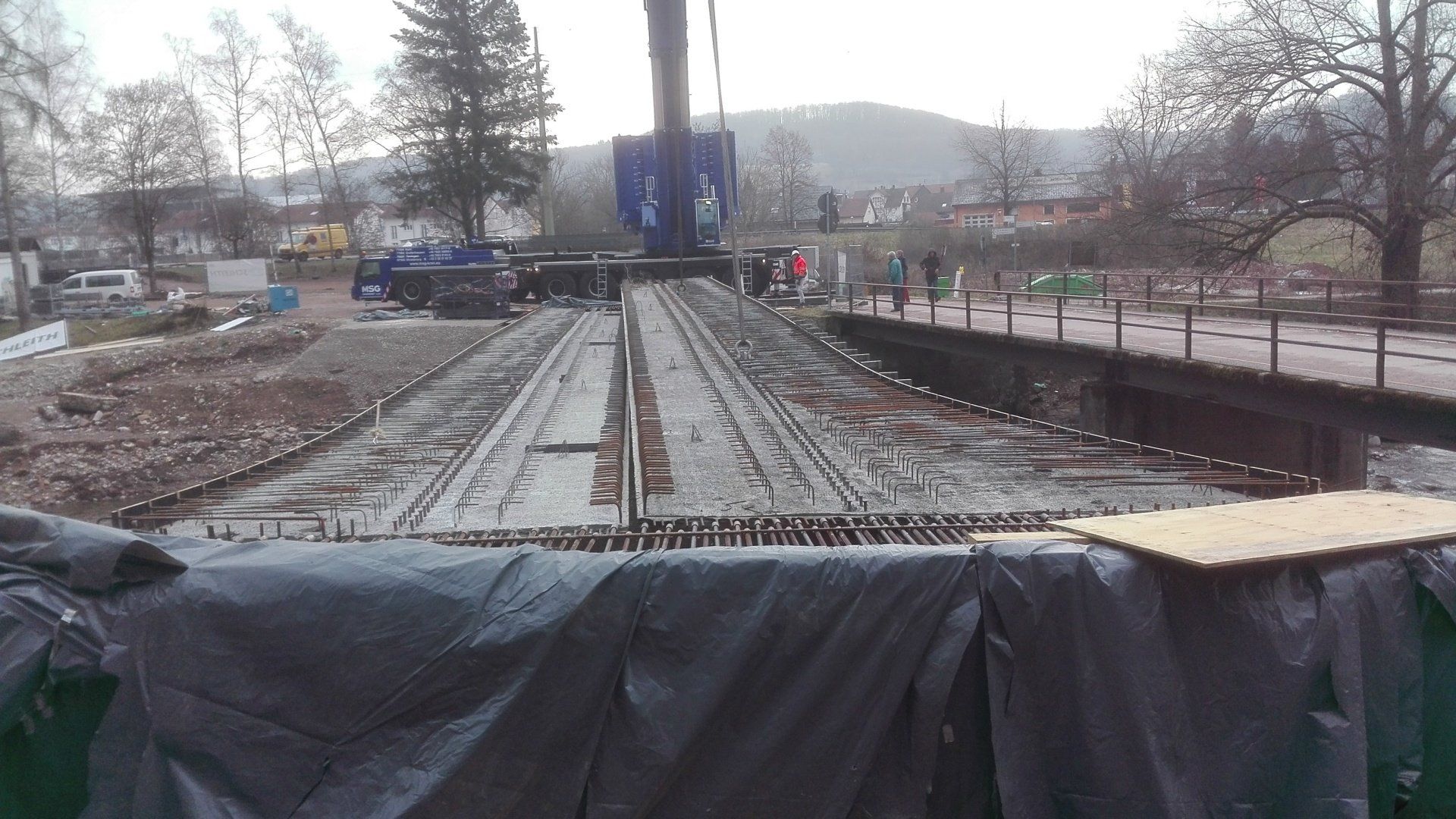 Eisenbahnbaustelle, auf der unter bedecktem Himmel neue Gleise durch ein schlammiges, eingezäuntes Gebiet verlegt wurden.