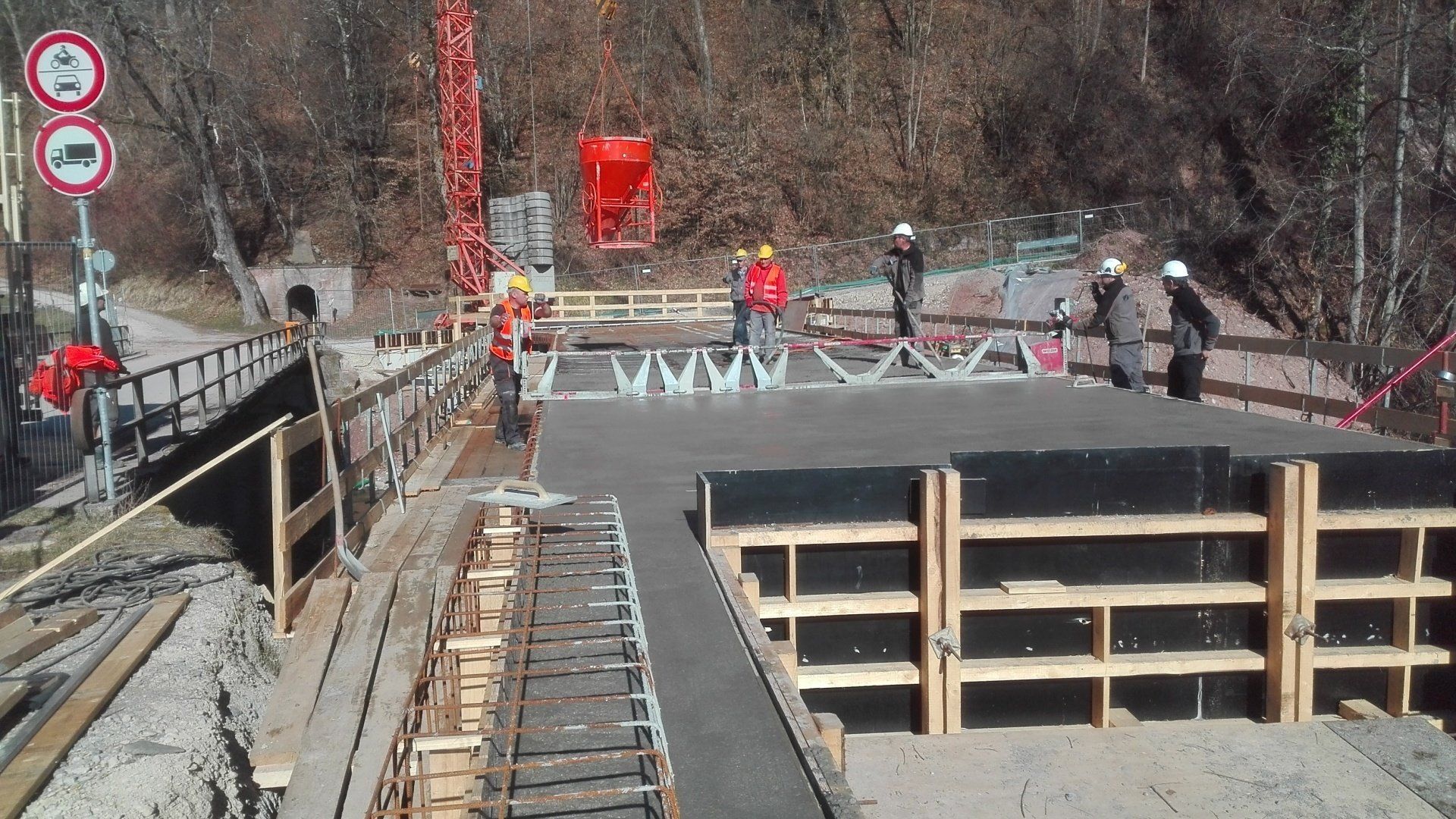 Teilweise errichtete Brücke mit Arbeitern, Geländern und Baustellenabsperrungen über eine Straße oder Schlucht